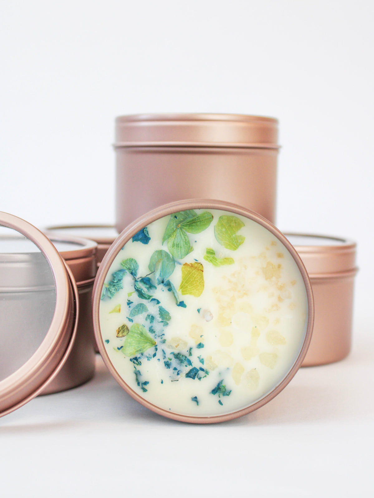 Botanical soy wax candle set in rose-gold tins with blue-green dried leaves in wax