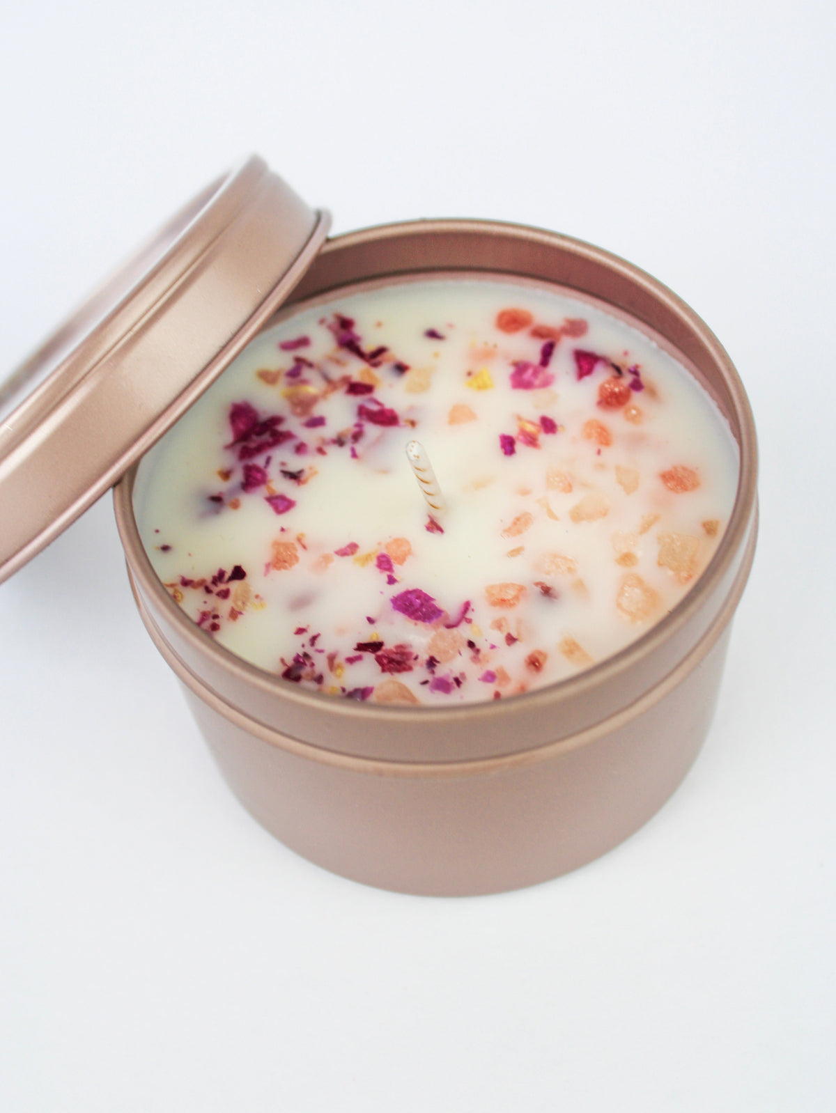 Single botanical soy wax candle in rose-gold tin with dried purple petals on wax