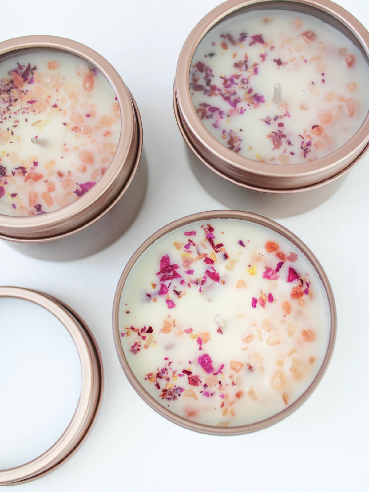 Botanical soy wax candles in rose-gold tins with dried flower petals on creamy wax
