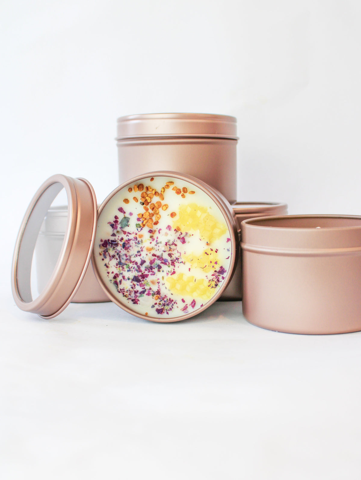 Rose-pink soy wax candle tin with open lid; colorful dried petals over yellow wax