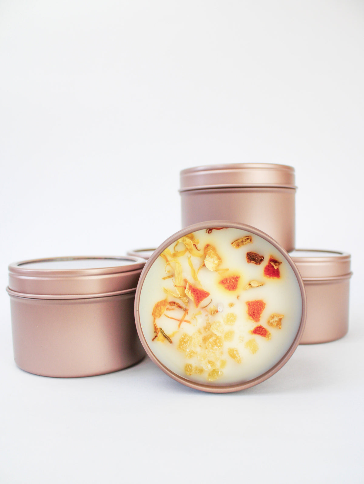 Botanical soy wax candle tins in rose-pink; open tin shows orange-yellow wax botanicals