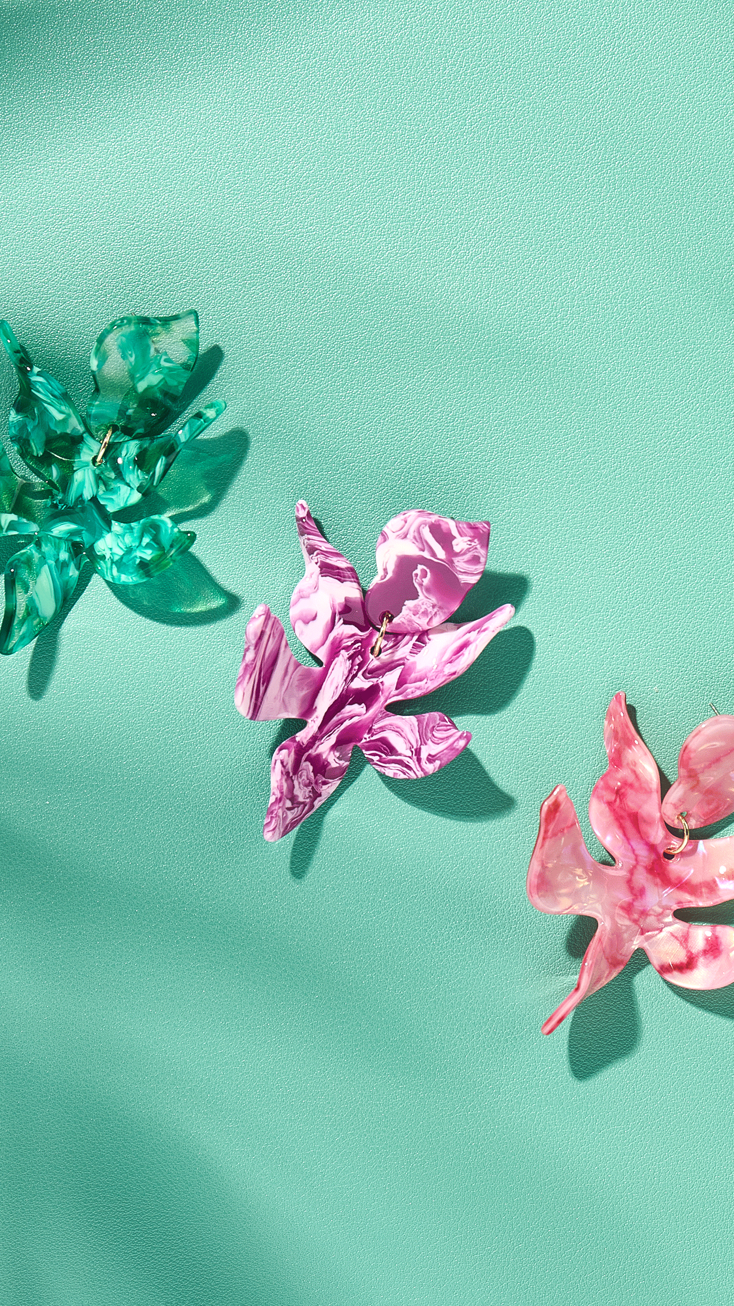 Pink floral earrings with layered petal shapes hanging against a blue background