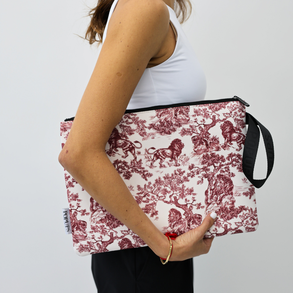 Toile-patterned laptop sleeve in maroon and white, worn with black shoulder strap