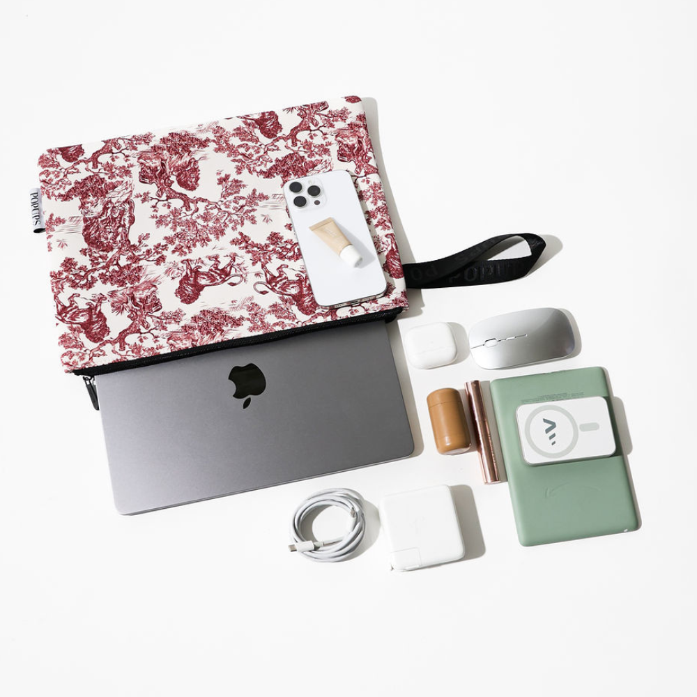 Maroon toile laptop sleeve with black zipper and strap, shown with small accessories