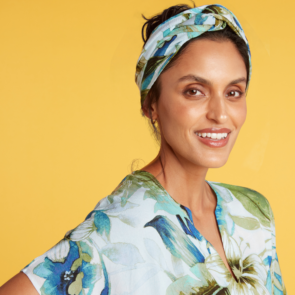 Tropical botanical print headwrap in blue and green worn over hair by a smiling woman