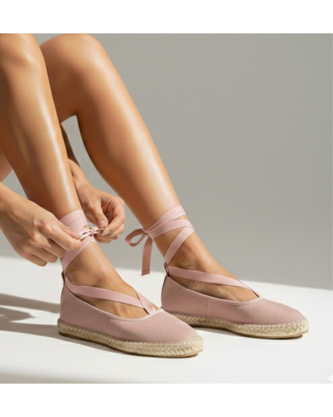 Pink suede ballet flats with ankle ties and braided jute soles, worn on feet