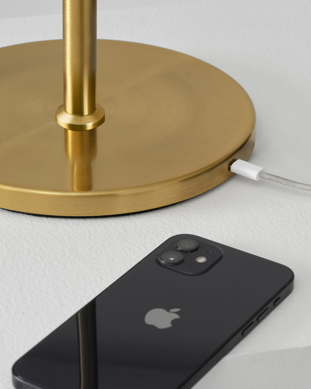 Gold lamp base with white power cord and brass stem beside smartphone on white surface