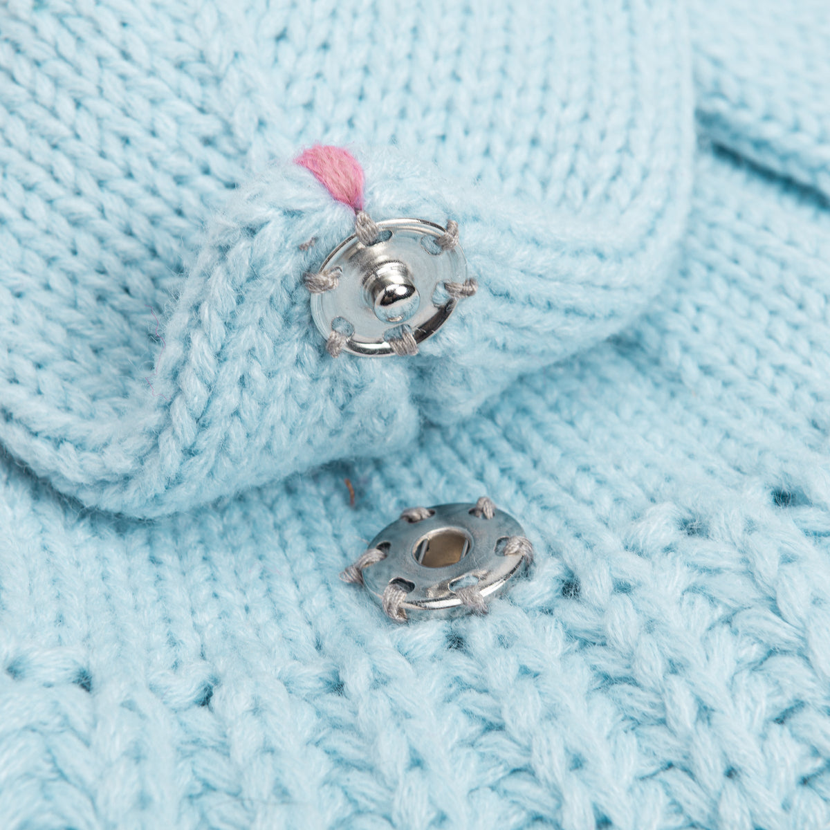 Close-up of the metal snap fastener on the pale blue knitted rabbit scarf