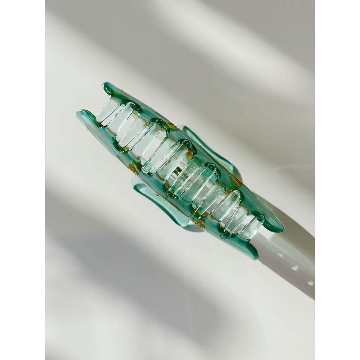 Goldfish hair claw clip, close side view of clear teal prongs and hinge