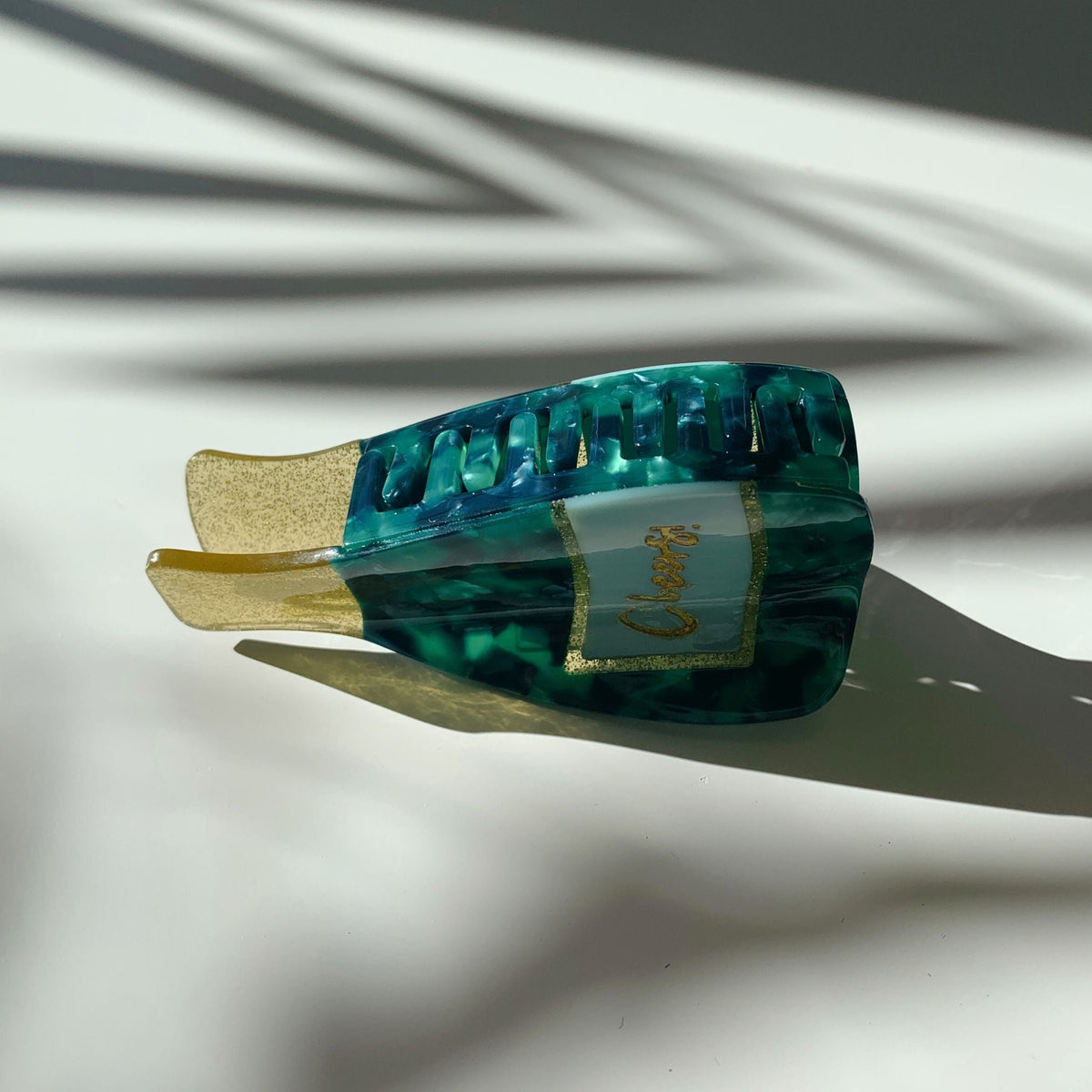 Teal marbled hair claw with gold glitter prongs and cream front label