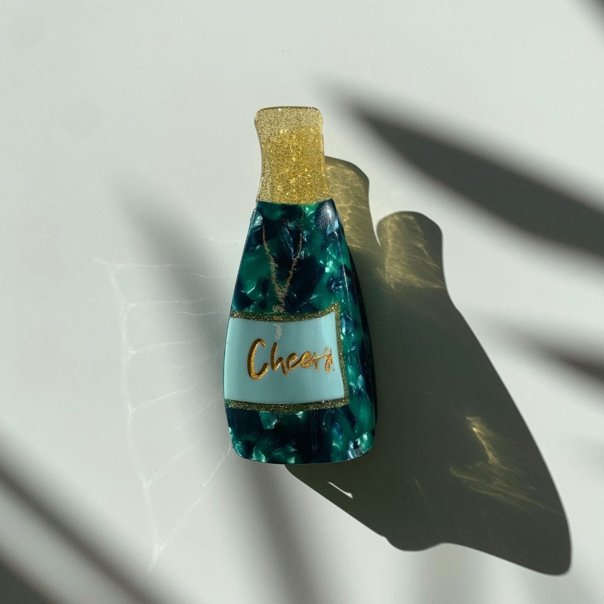 Teal marbled hair claw with gold glitter top and cream center label