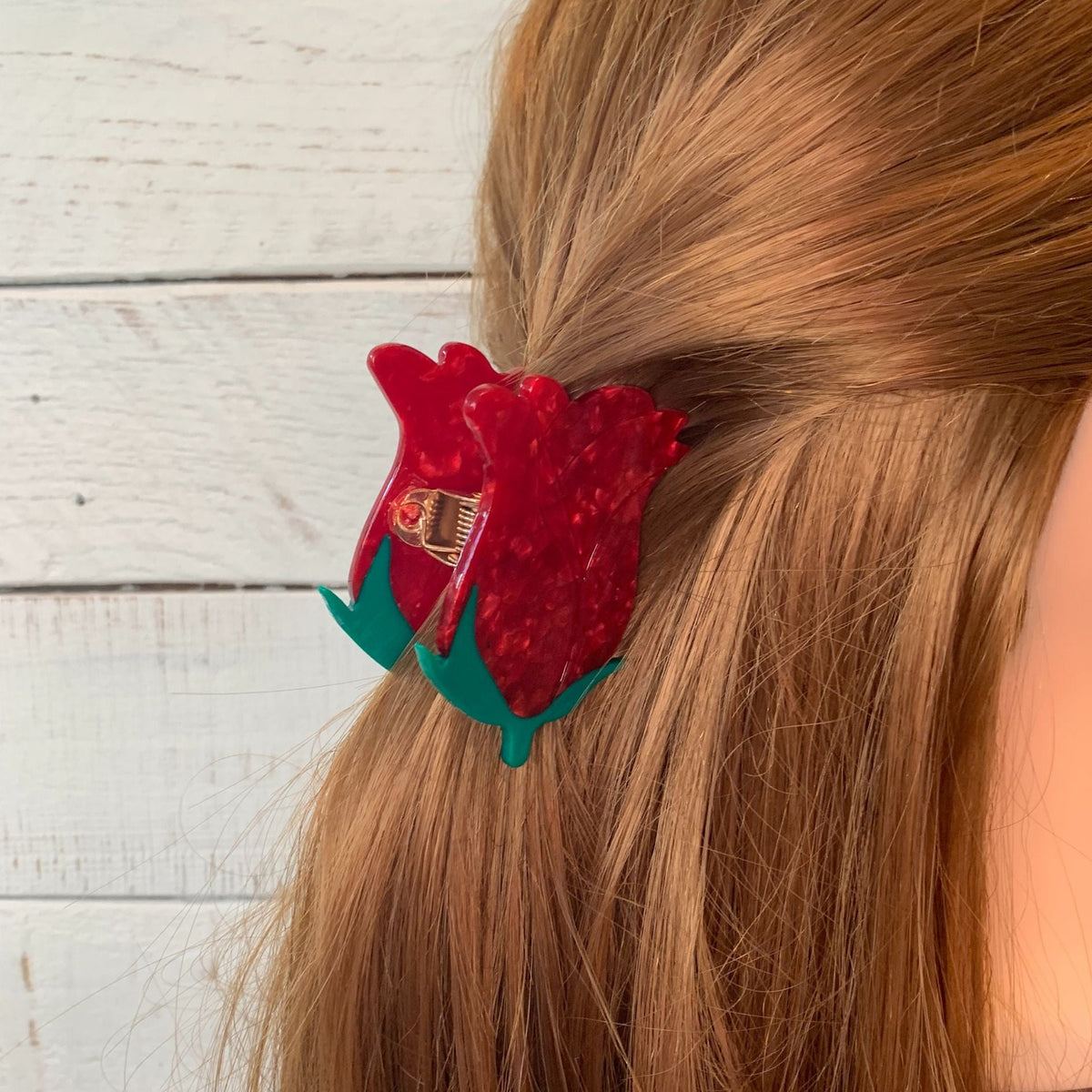 Red rosebud hair claw clip with green leaves, worn on light brown hair