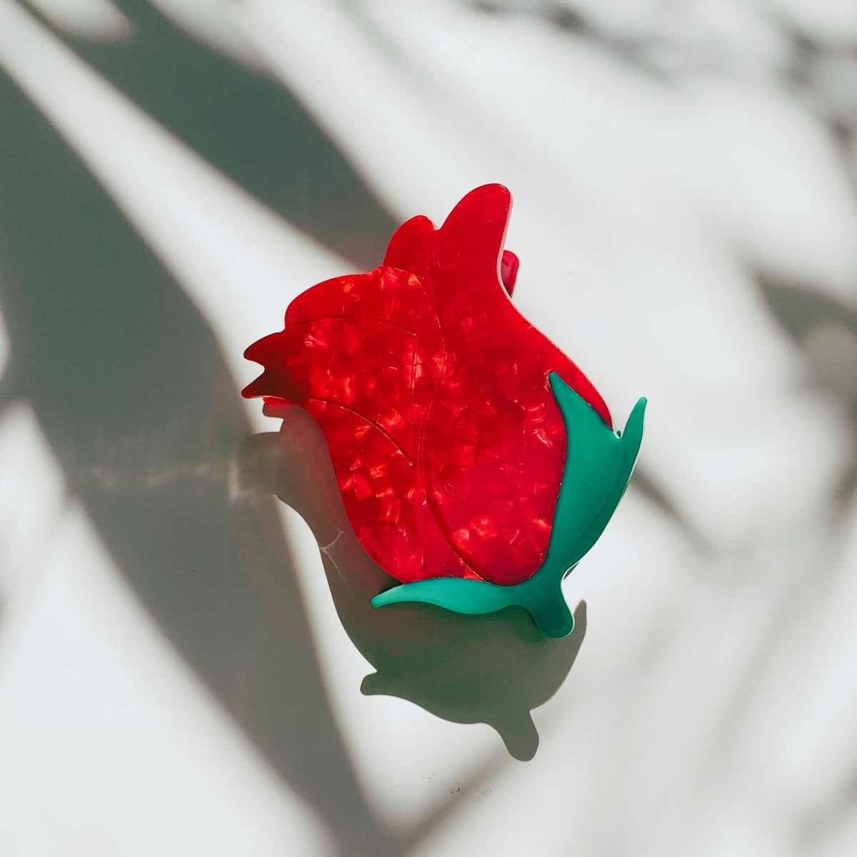 Red rosebud hair claw clip with green leaves, angled side view