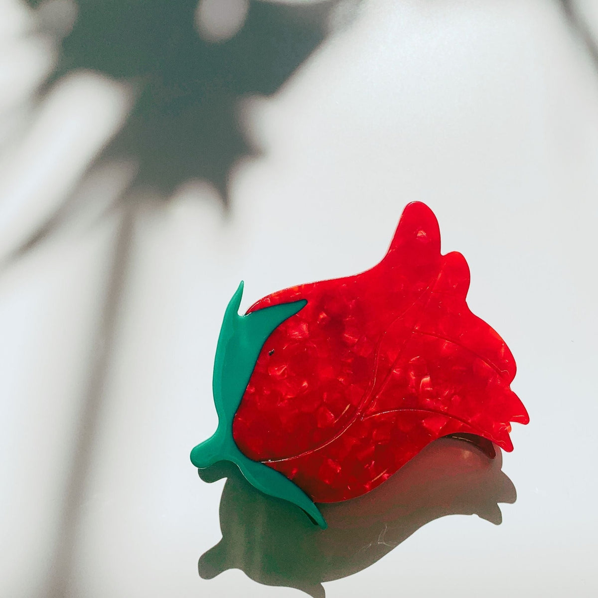 Red rosebud hair claw clip with green leaves, close-up