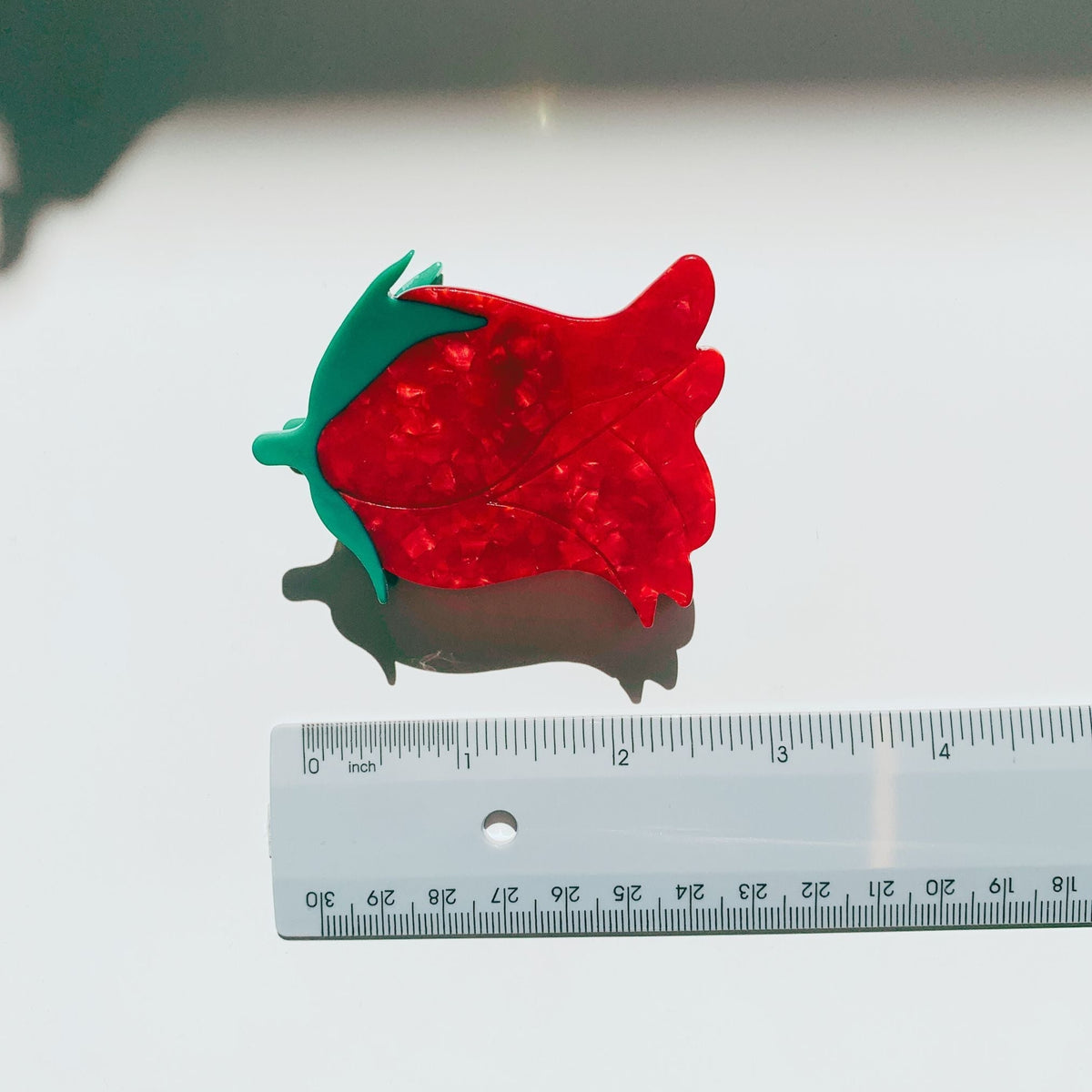 Red rosebud hair claw clip with green leaves next to a ruler for size