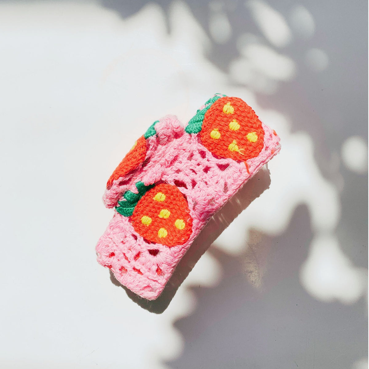 Pink crocheted hair claw with orange strawberry face details and green leaves
