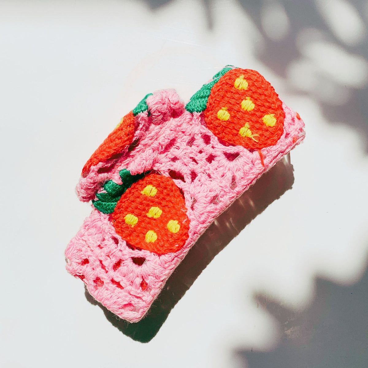 Pink crocheted hair claw with orange strawberry faces and green leaf accents