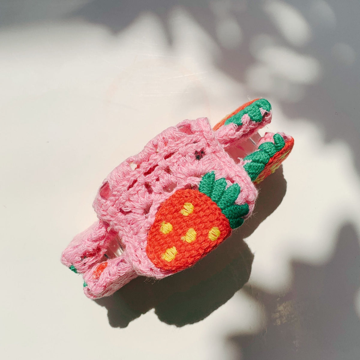 Pink strawberry crocheted hair claw, angled view with green leaf details