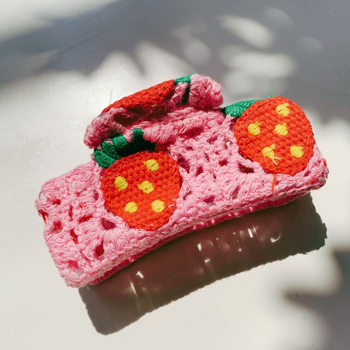 Pink crochet hair claw with two orange strawberry appliques and green leaf stems