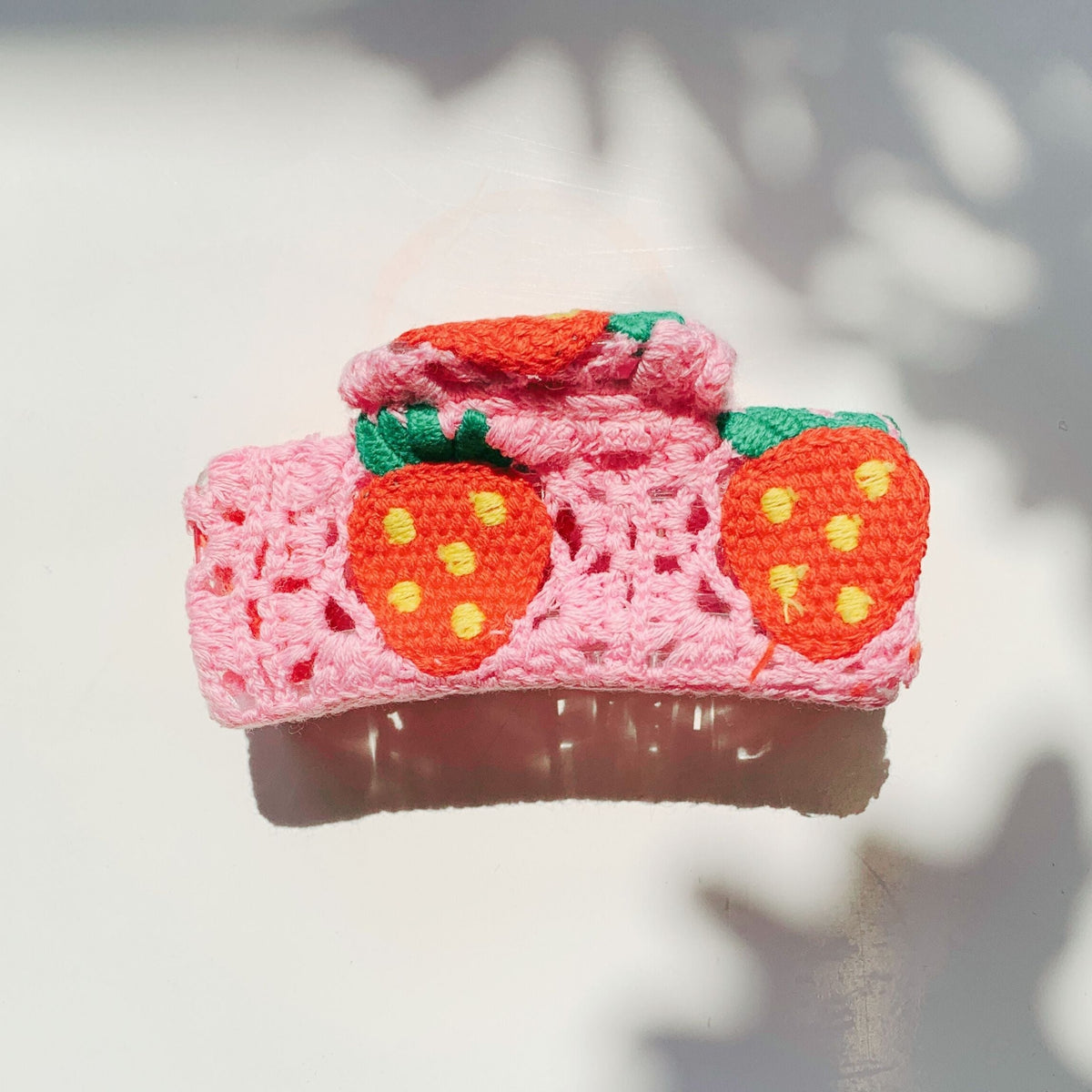 Pink crocheted hair claw featuring two orange strawberries and green leaf accents