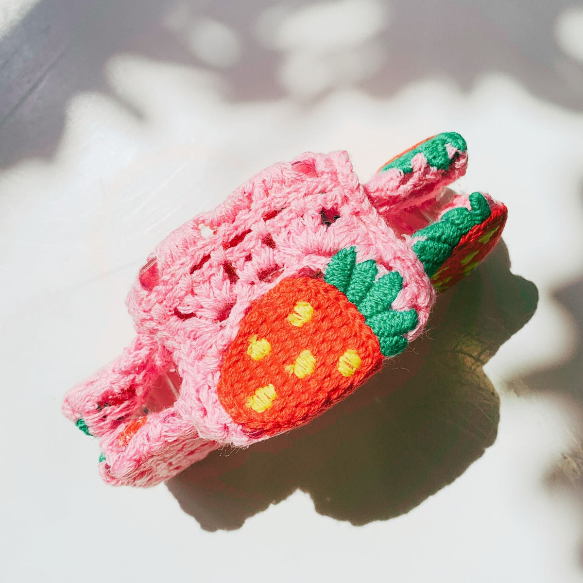 Pink crocheted hair claw with orange strawberries and green leaves, side view