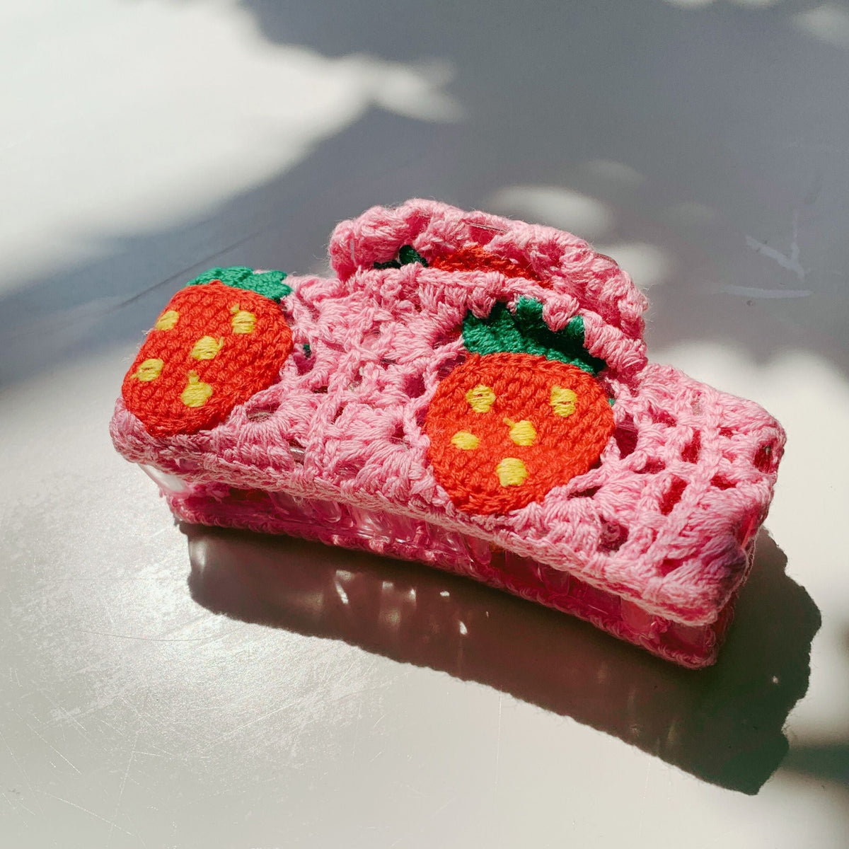 Crochet pink hair claw with two orange strawberry appliques and green leaves