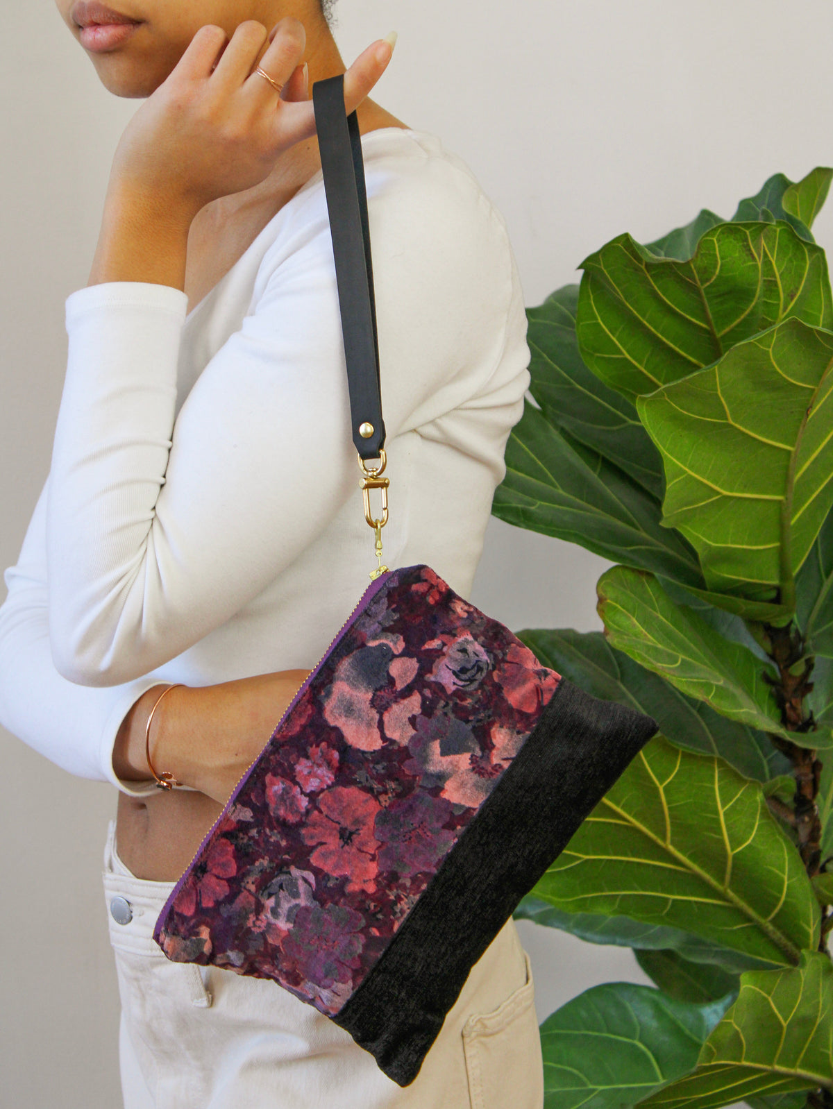 Purple floral velvet wristlet with black base, carried on wrist with gold chain strap.