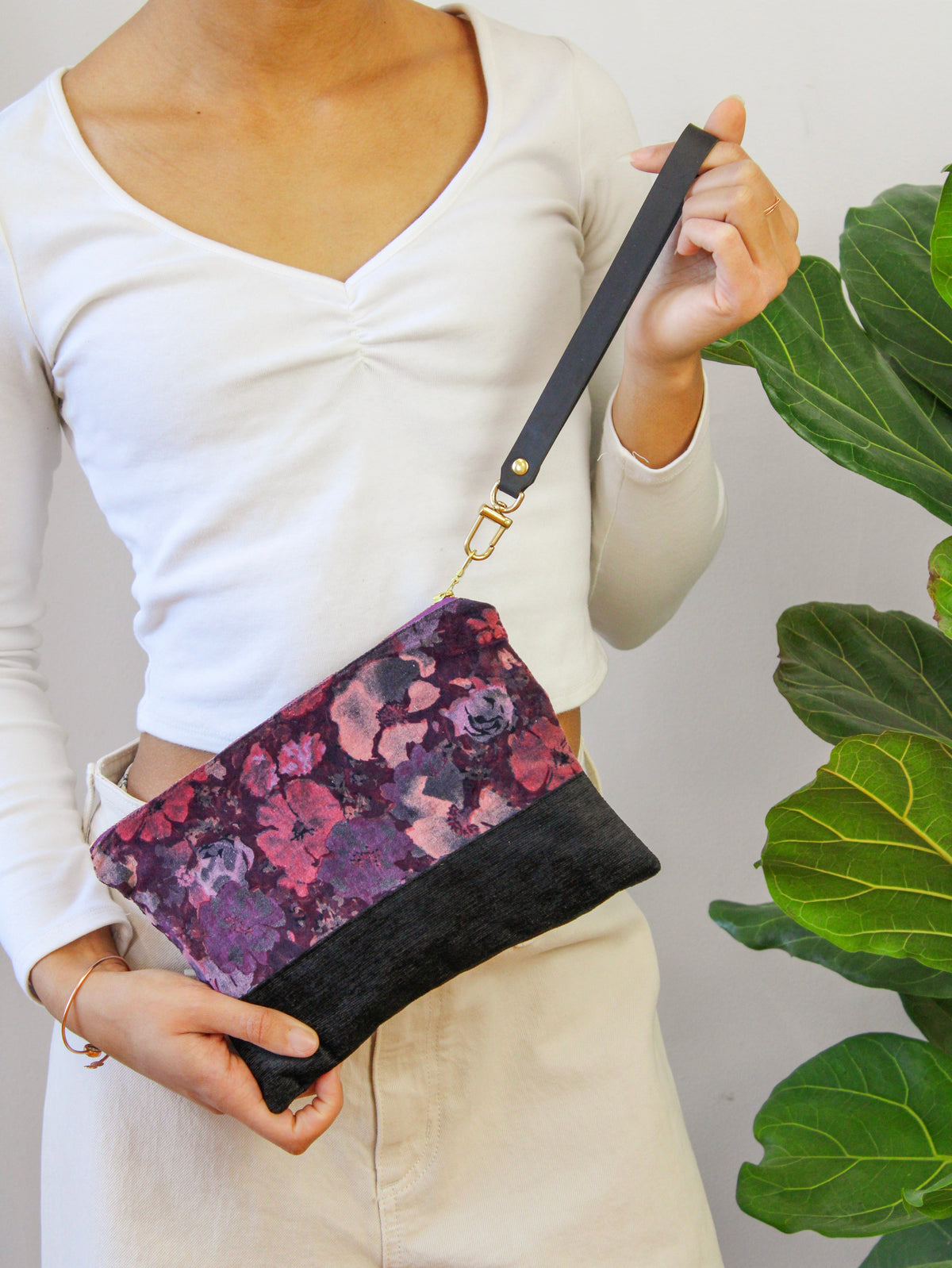 Velvet wristlet worn crossbody, purple floral print with black base and gold hardware.
