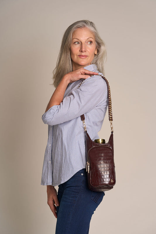 Merlot faux croc HydroBag crossbody worn by woman, gold-tone hardware and tassel detail