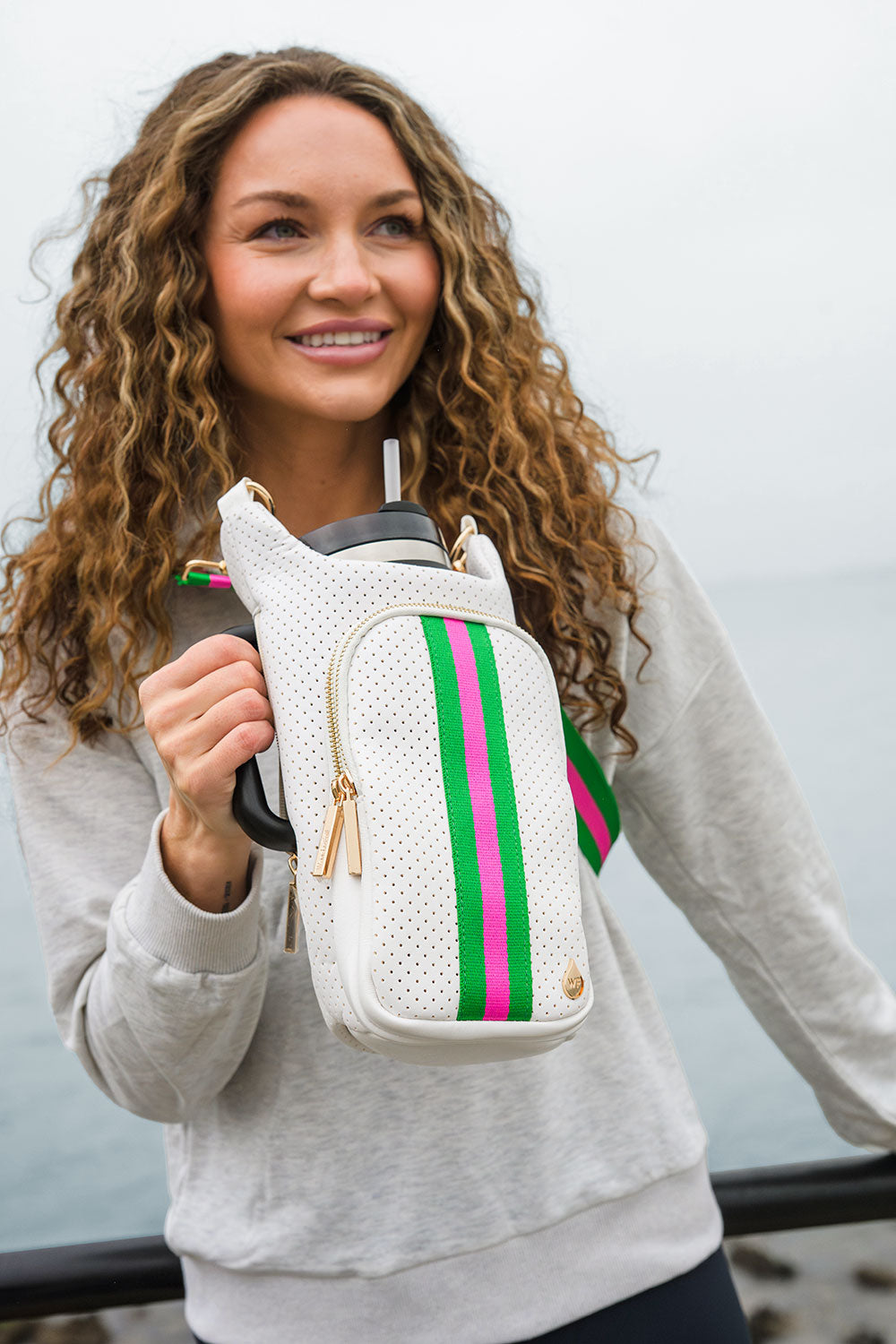 White striped HydroBag held by a woman, showing perforated fabric and gold zip detail