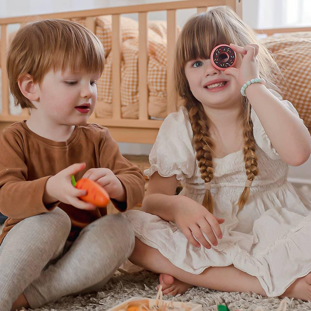 Wooden play food including a toy doughnut and carrot held by children