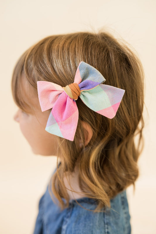 Petite plaid hair bow worn in brown hair; pink, teal, blue, and orange plaid