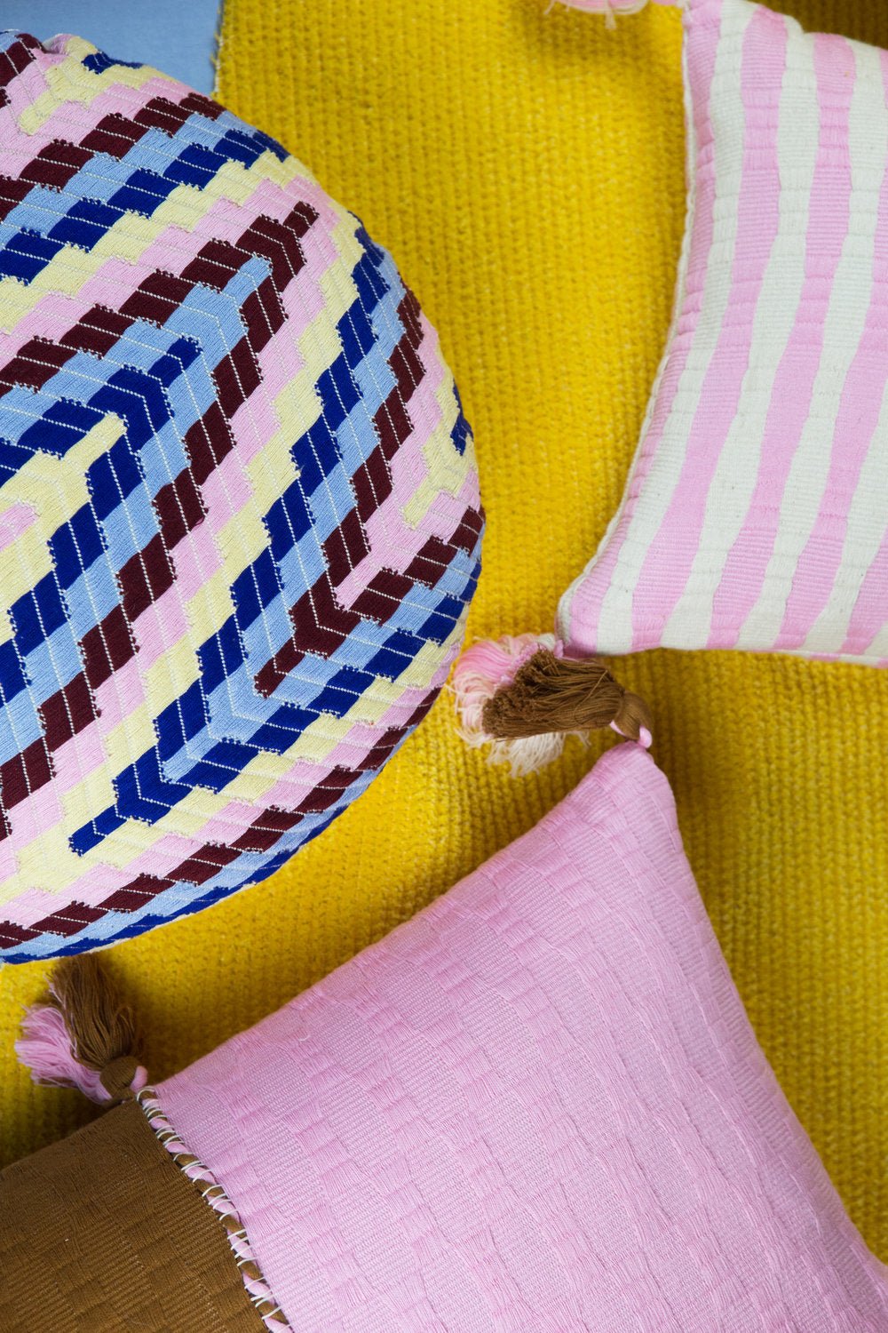 Square throw pillow with blue, pink, and white striped pattern and fringed trim