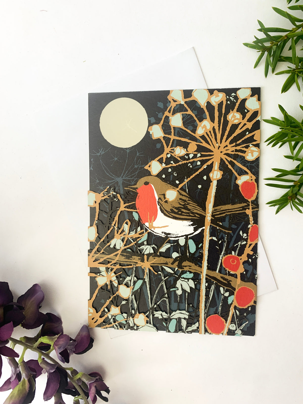 Christmas card front with robin, glowing moon, branches, and red berry accents