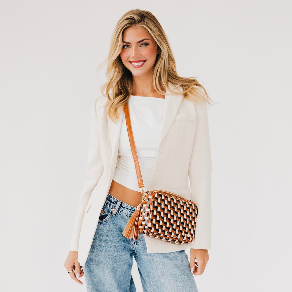 Woven checkered camera crossbody bag in dark brown with tan leather strap and tassel pull.