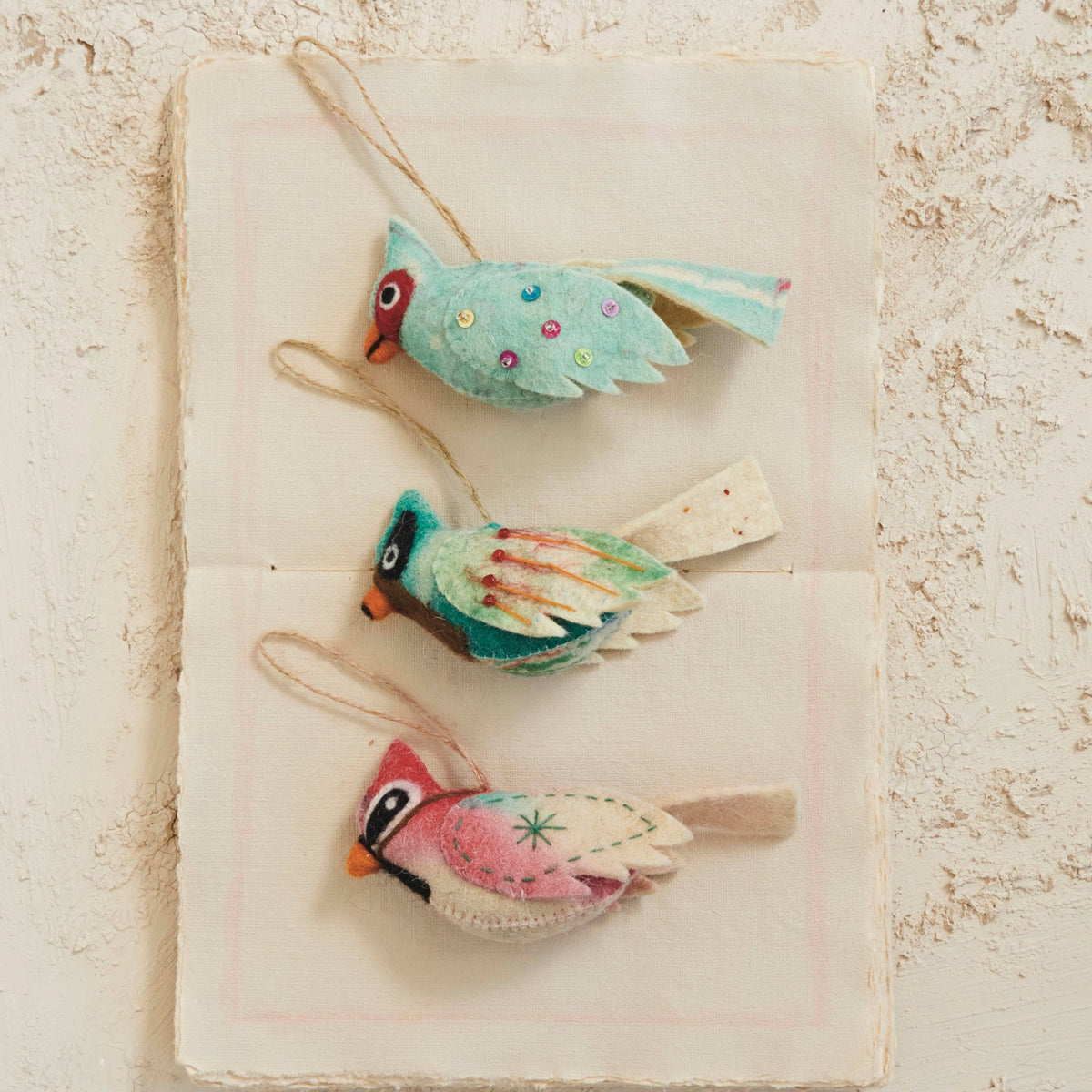 Wool felt bird ornaments on cloth, teal and blue wings plus red bird with string