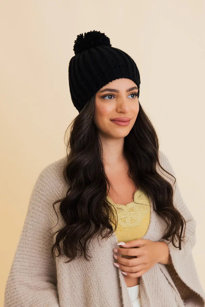 Black chunky cable knit pom beanie, angled side view with pom top
