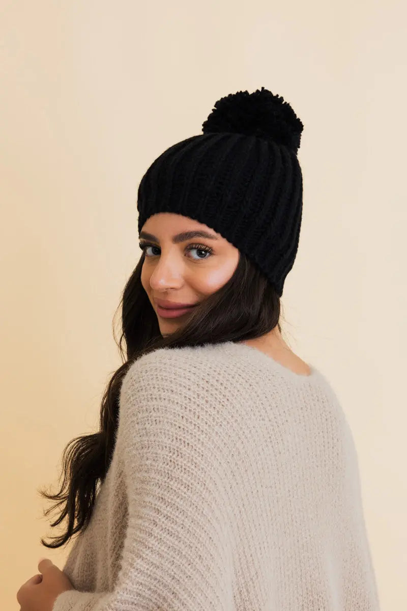 Black cable knit pom beanie viewed from the back with ribbed cuff