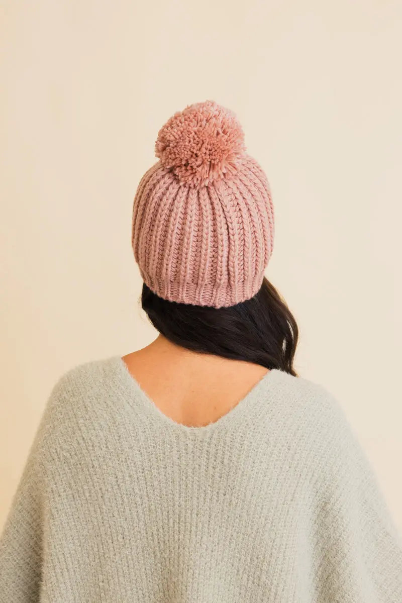 Blush pink cable knit pom beanie viewed from the back with ribbed cuff