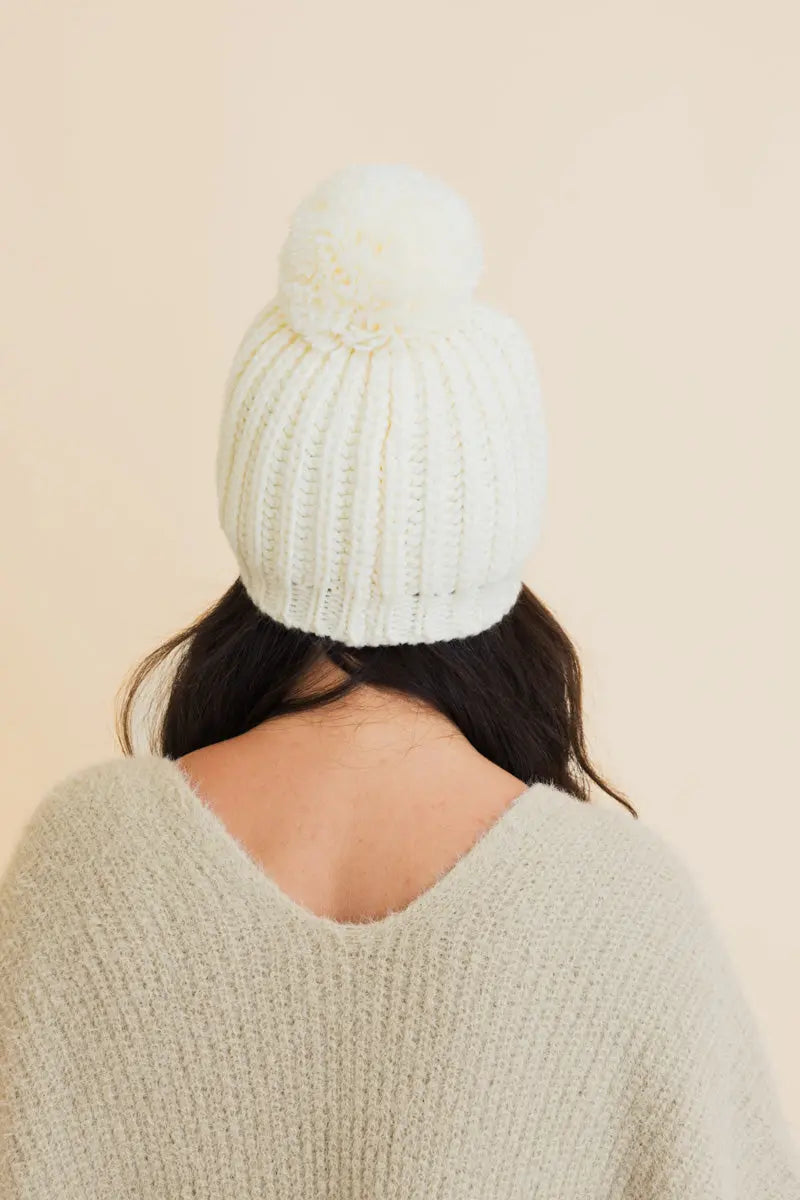 Ivory chunky cable-knit beanie with folded cuff and large pom-pom.