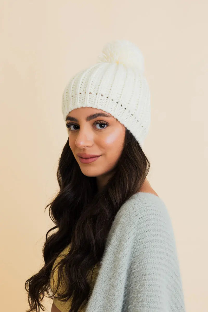 Ivory cable-knit pom beanie with ribbed cuff and soft top pom.
