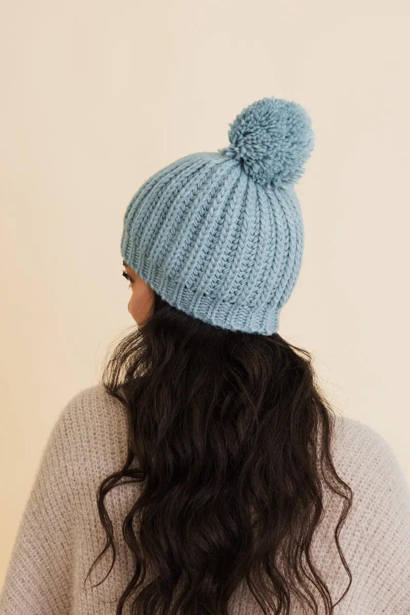 Sea blue cable-knit pom beanie shown from back with large pom on top.