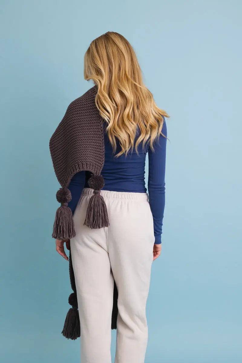 Brown knit scarf with long drape and hanging tassel pom-poms on the ends