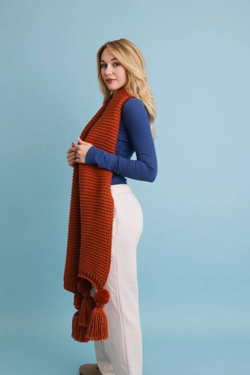 Rust orange knit scarf with long fringed ends and pom-pom tassels