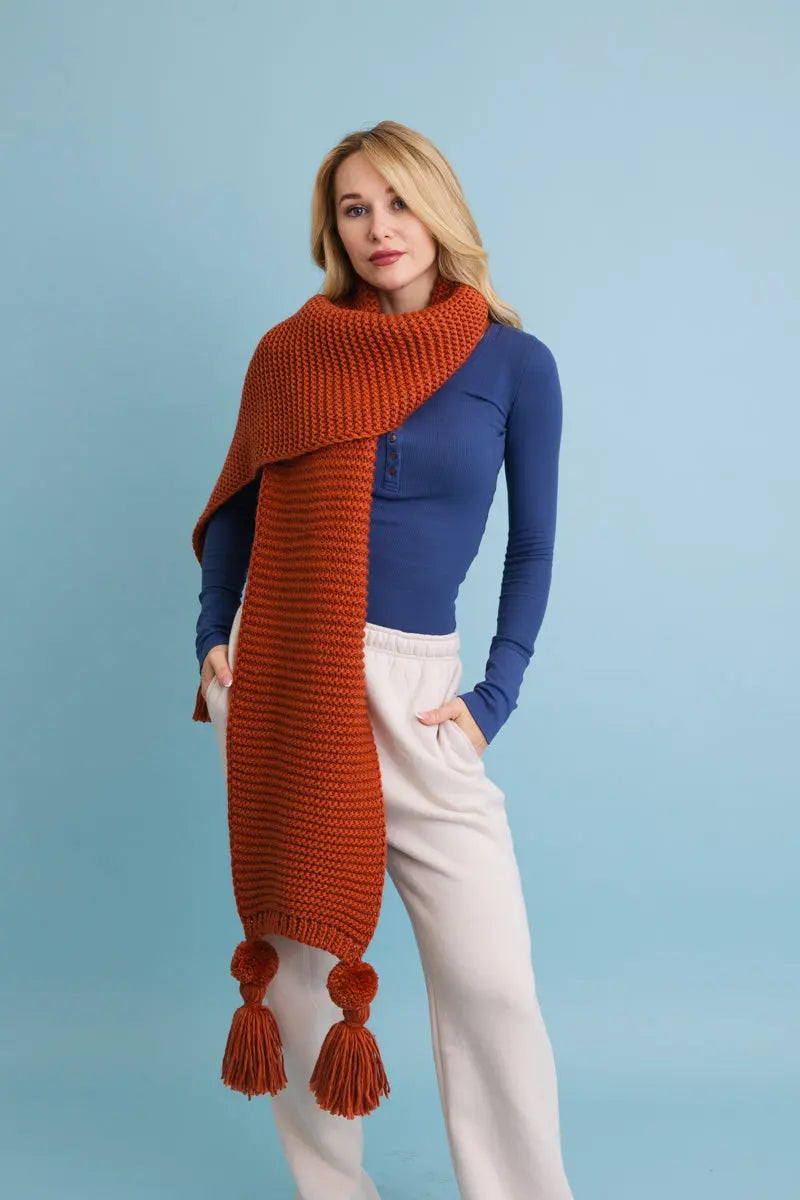 Rust orange knit scarf with long ends and tassel pom-poms on both sides