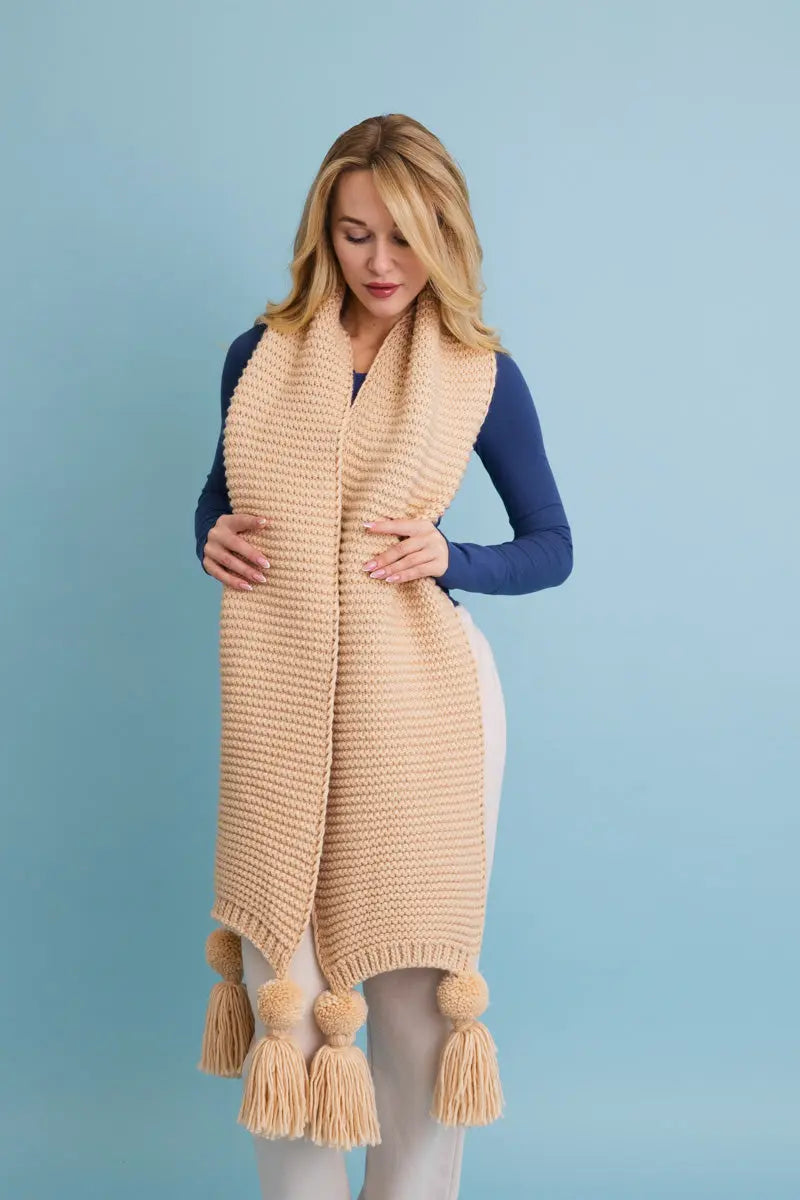 Tan knit scarf with openwork knit and pom-pom tassels along bottom edge