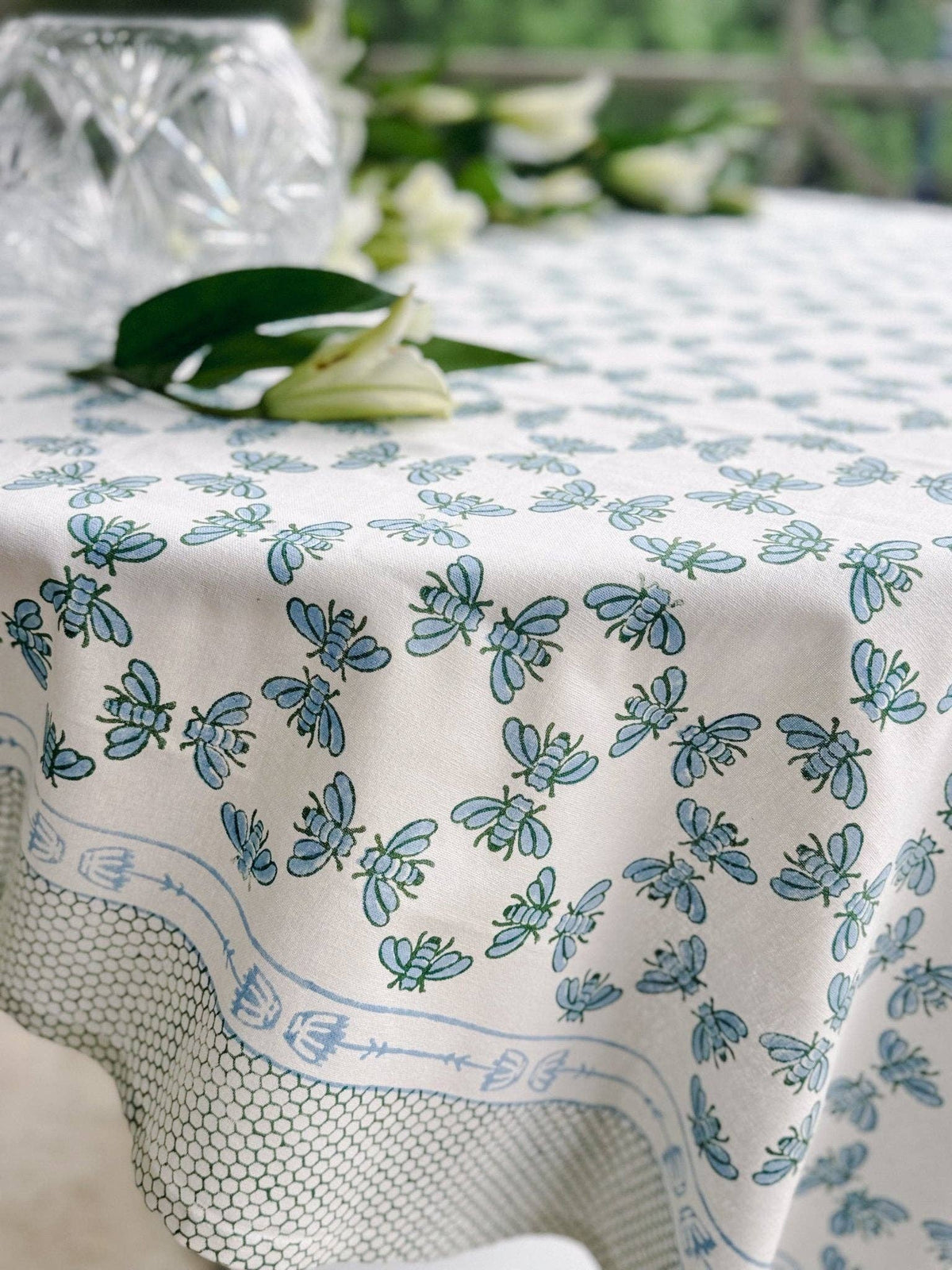 Table throw with blue-and-sage floral print on white fabric, stitched edge and border.