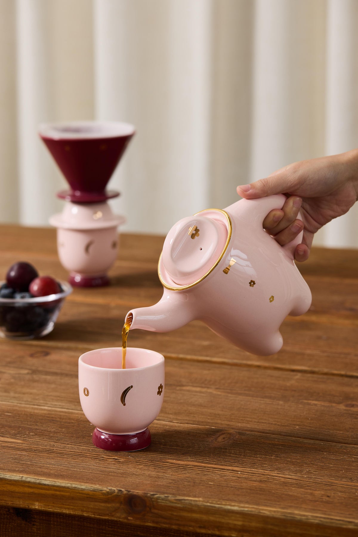 Pink porcelain teapot pouring coffee into matching cup with another cup nearby