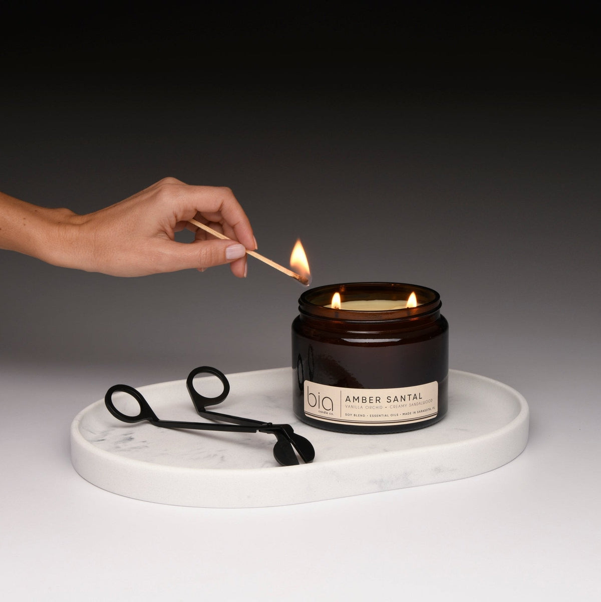 Amber glass soy candle jar with flame, hand lighting with match