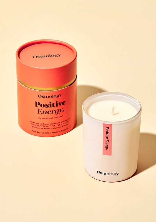 Orange and white scented candles in cylindrical tins, orange label facing up (Osmology)
